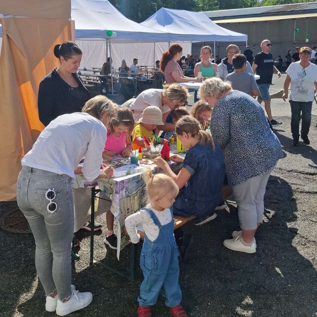 Společné rodinné tvoření u plně obsazeného stolu na venkovním firemním teambuildingu
